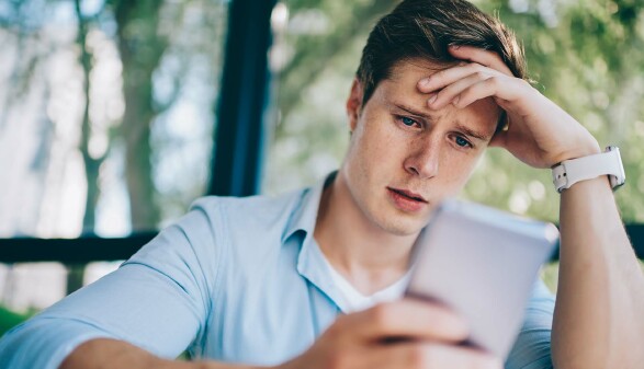 Ein junger Mann schaut mit besorgtem Gesichtsausdruck auf sein Smartphone.