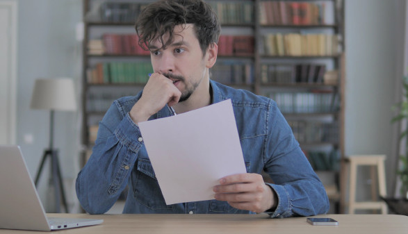Nachdenklicher Mann sitzt mit Zettel vor Notebook