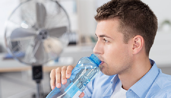Mann trinkt von Wasserflasche und Ventilator spendet kühle Luft