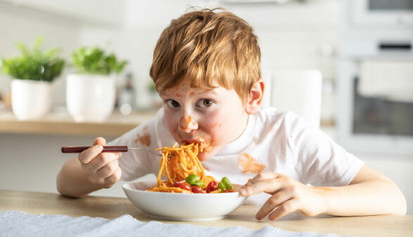 Ein kleiner Junge isst Spaghetti Bolognese.