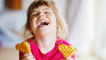 Ein lachendes M&auml;dchen mit je einem Keks in der Hand.