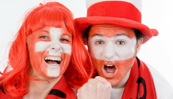 Ein &ouml;sterreichischer und ein schweizer Fu&szlig;ballfan jubelnd in rot-wei&szlig;-roter Fankleidung 