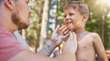 Vater schmiert seinen Sohn im Gesicht und am Oberk&ouml;rper mit Sonnencreme ein.