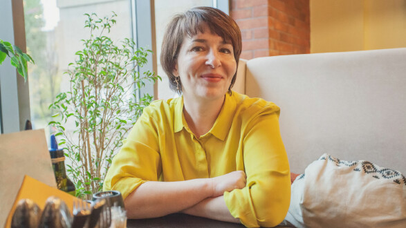 Frau sitzt l&auml;chelnd an einem Tisch im Caf&eacute; oder Wohnzimmer und blickt nachdenklich zur Seite &ndash; Symbolbild f&uuml;r Beratung, Vorsorgeplanung oder pers&ouml;nliche Entscheidungen.