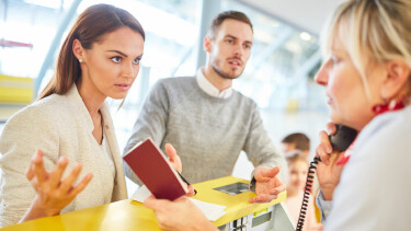 Ein Paar diskutiert am Flughafen-Schalter mit einer Dame &uuml;ber die G&uuml;ltigkeit der Reisep&auml;sse.