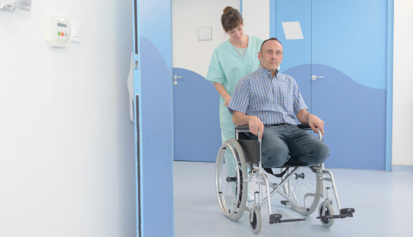 Mann mit zwei amputierten Beinen im Rollstuhl, geschoben von einer Pflegehelferin