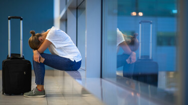 Ersch&ouml;pfte junge Frau wartet mit ihrem Trolley am Flughafen auf ihren versp&auml;teten Flug.
