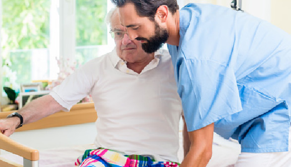 Pfleger hilft altem Mann aus dem Krankenbett