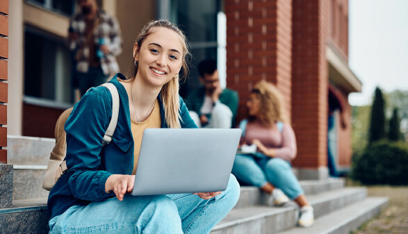 Sch&uuml;lerin sitzt mit Laptop auf Stufe vor der Schule