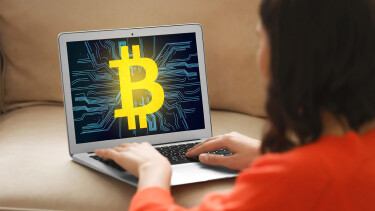 Frau sitzt vor Laptop mit Bitcoin-Zeichen