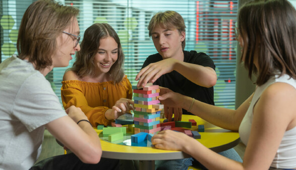 Jugendliche bauen gemeinsam an einem Turm aus Holzklötzen