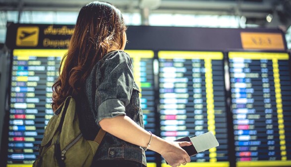 Junge Frau schaut auf Flugzeitentafel am Flughafen