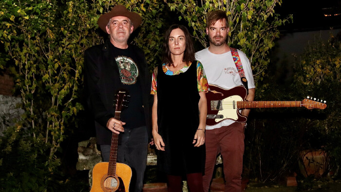 Drei Personen stehen draußen vor dichter Gartenvegetation. 