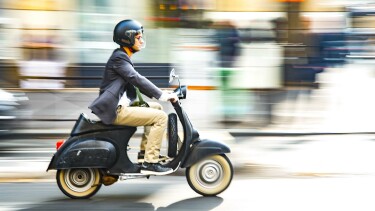 Ein junger Mann mit schwarzem Helm f&auml;hrt mit dem Moped durch die Stadt.