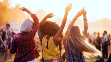 Drei junge Menschen, von hinten zu sehen, feiern tanzend auf einem Festival.