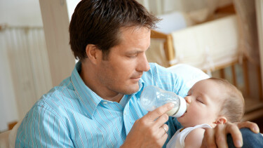 Vater f&uuml;ttert sein Baby mit einer Milchflasche im Wohnzimmer.
