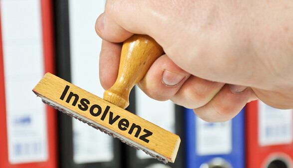 Eine Hand h&auml;lt einen Holzstempel, auf dem das Wort &bdquo;Insolvenz&ldquo; steht.