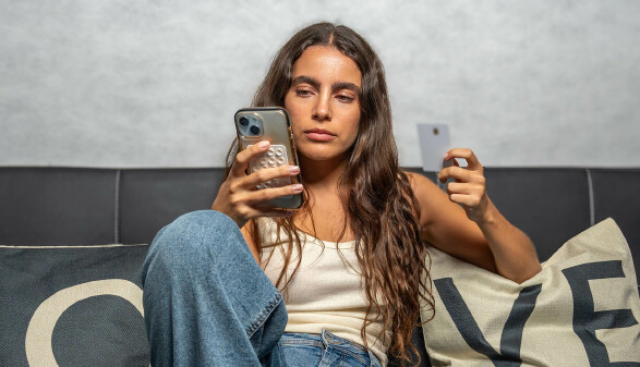 Frau sitzt auf Couch und tätigt Überweisung mit Handy