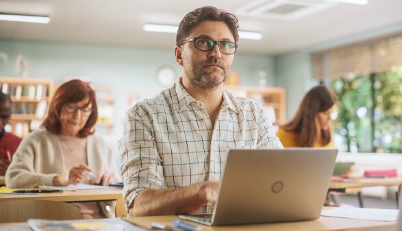 Mann arbeitet an einem Laptop in einem Kursraum.